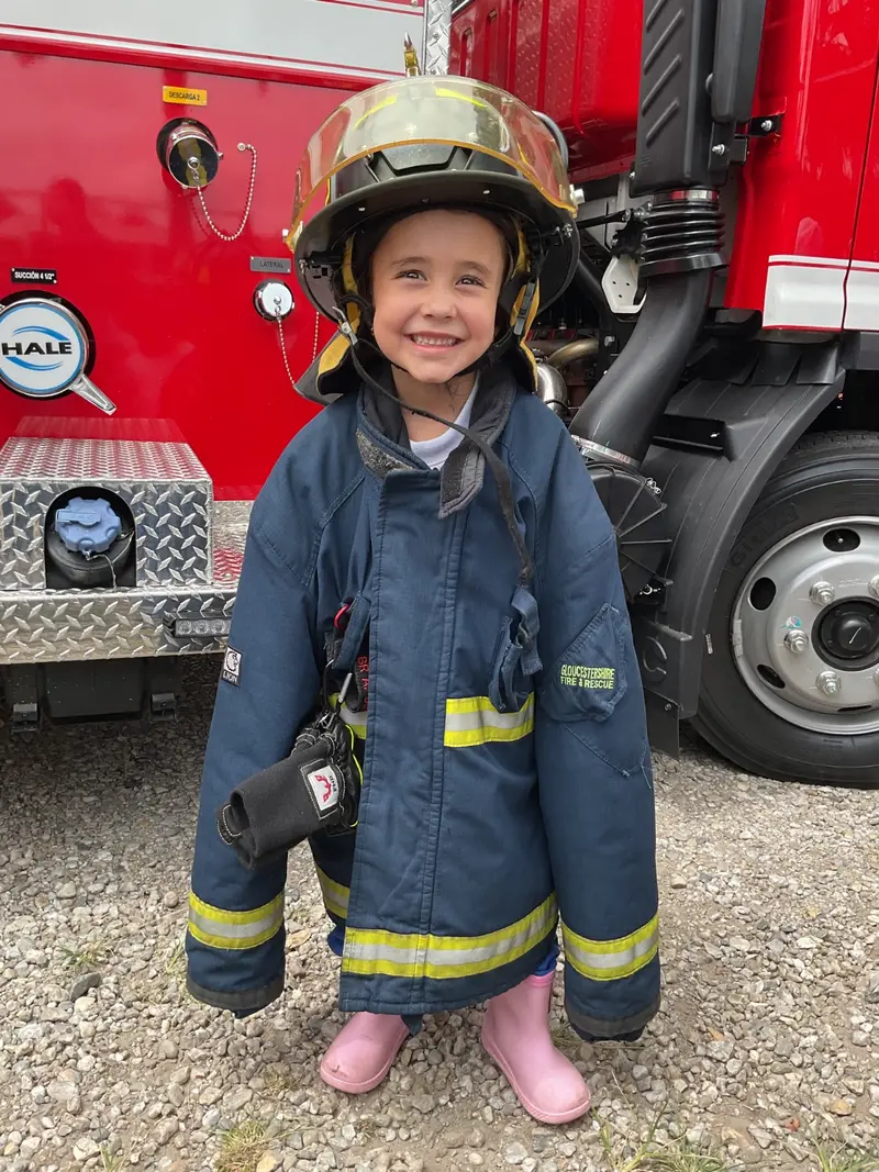 Niña de preescolar sonriendo con el traje de bombero durante la visita al cuerpo de bomberos